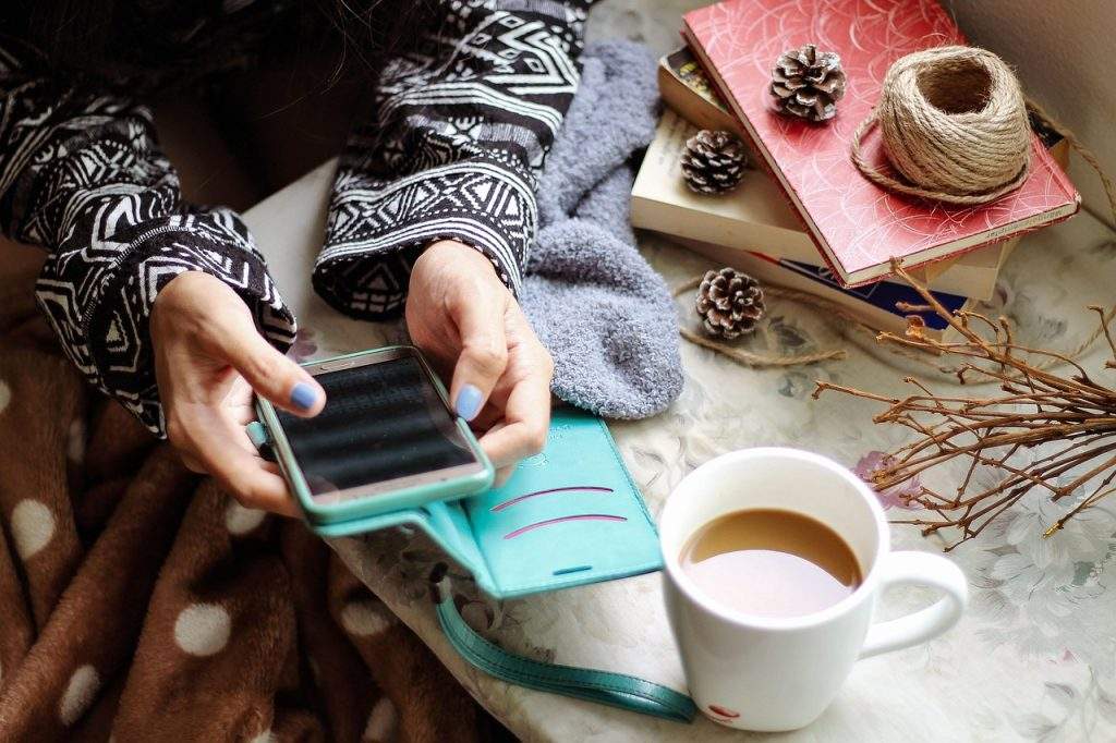 Una ragazza che guarda i social sullo smartphone con un caffè